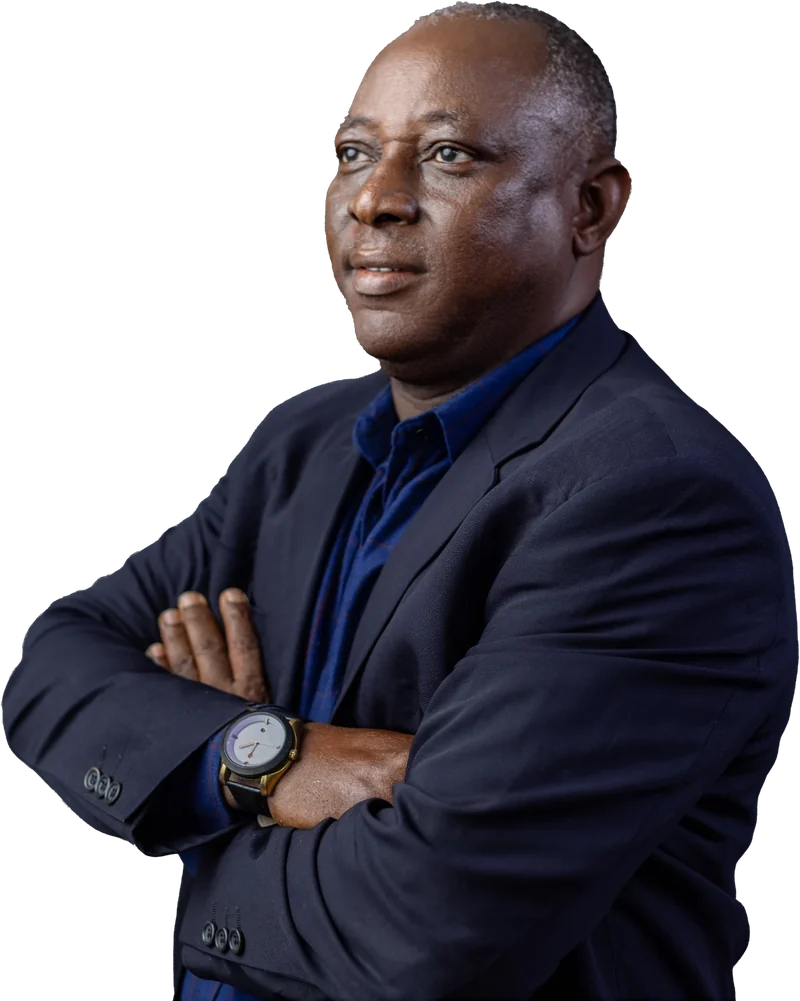 Kunle Olatunji ní aṣọ dúdú àti ẹ̀wù búlúù, ó ká ọwọ́ mọ́ àyà, ó ń wo ẹ̀gbẹ́